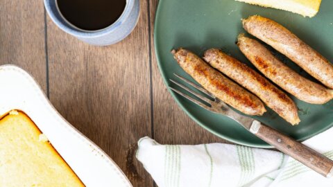 Overhead view of sausage links, cornbread and coffee on a wooden table.