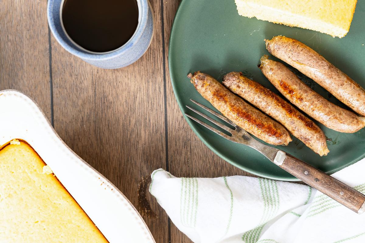 Overhead view of sausage links, cornbread and coffee on a wooden table.