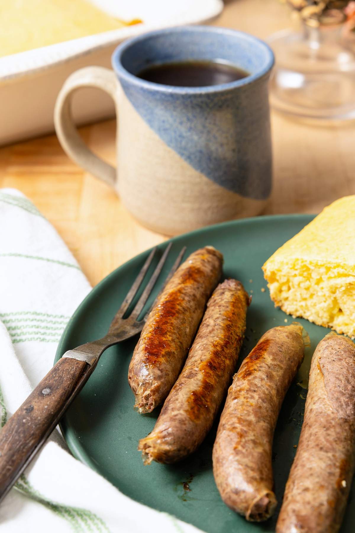 Browned sausage links served with cornbread and a blue mug of coffee.