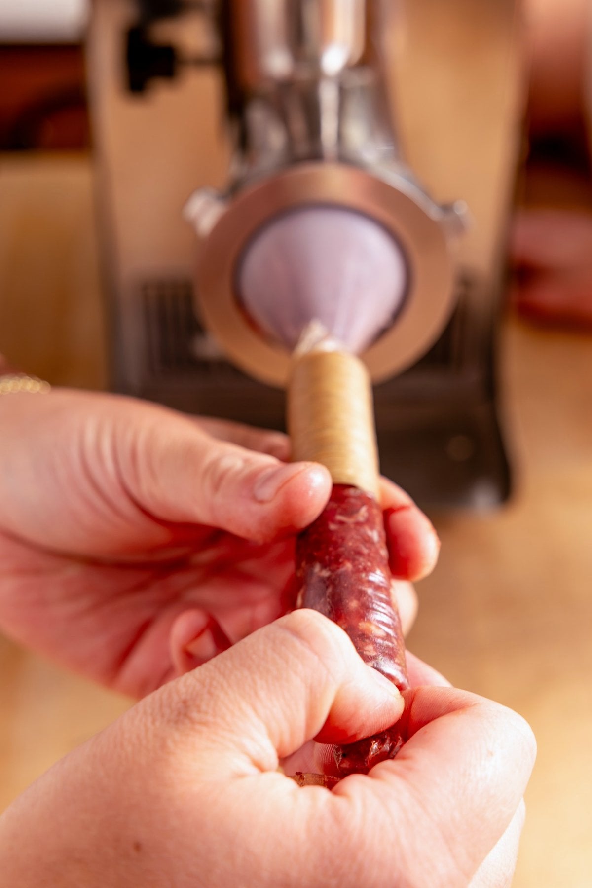 Hands guiding a sausage casing over the stuffer nozzle as it fills with meat.