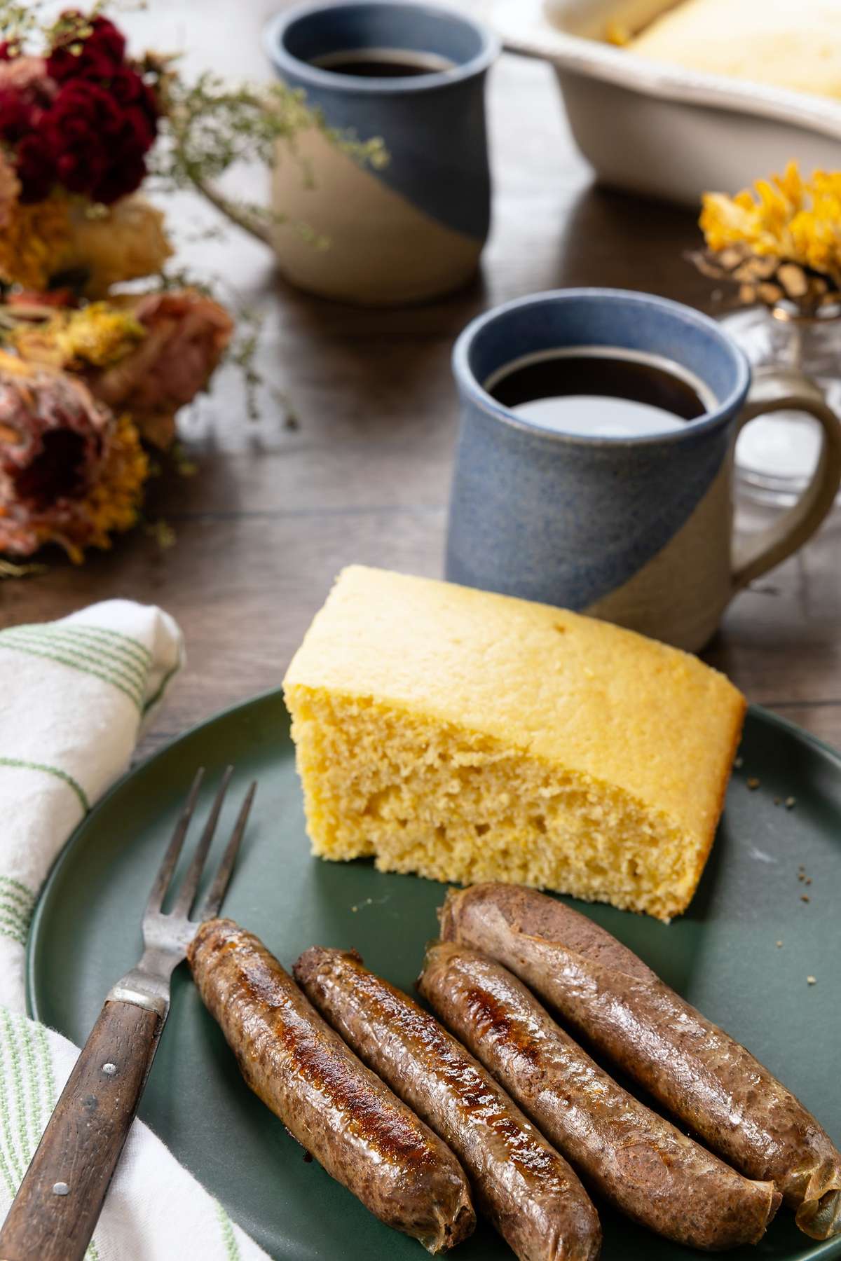 Cooked sausage links and cornbread on a green plate beside a mug of coffee.