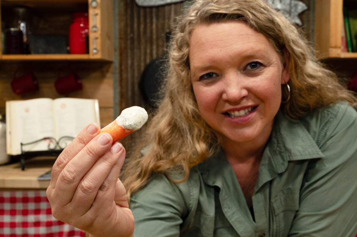 A woman taking a bite out of a veggie dipped in buttermilk ranch dressing.