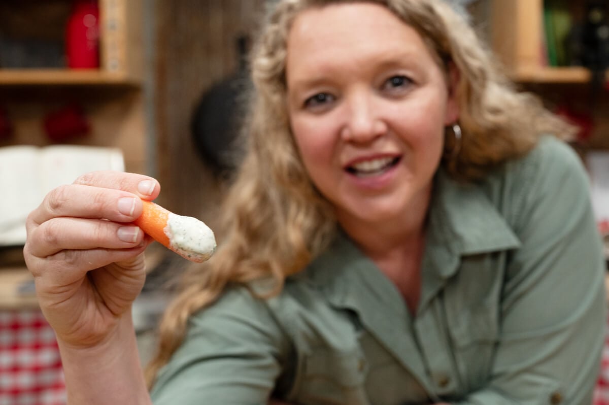 A woman taking a bite out of a veggie dipped in buttermilk ranch dressing.