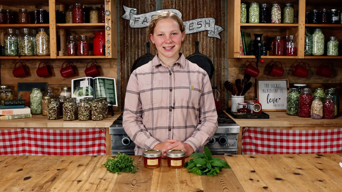 A young girl with herbal honey and fresh herbs on the counter.