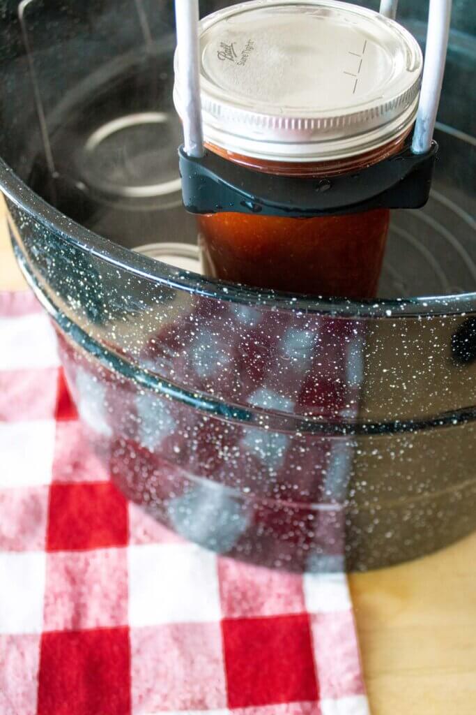 A jar lifter holding a jar of bbq sauce over a water bath canner.