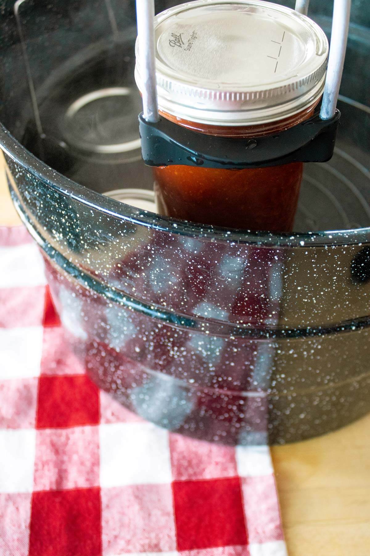 A jar lifter holding a jar of bbq sauce over a water bath canner.