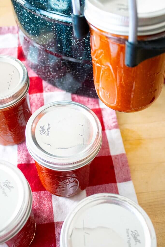 A jar lifter pulling a jar of BBQ sauce out of a water bath canner.