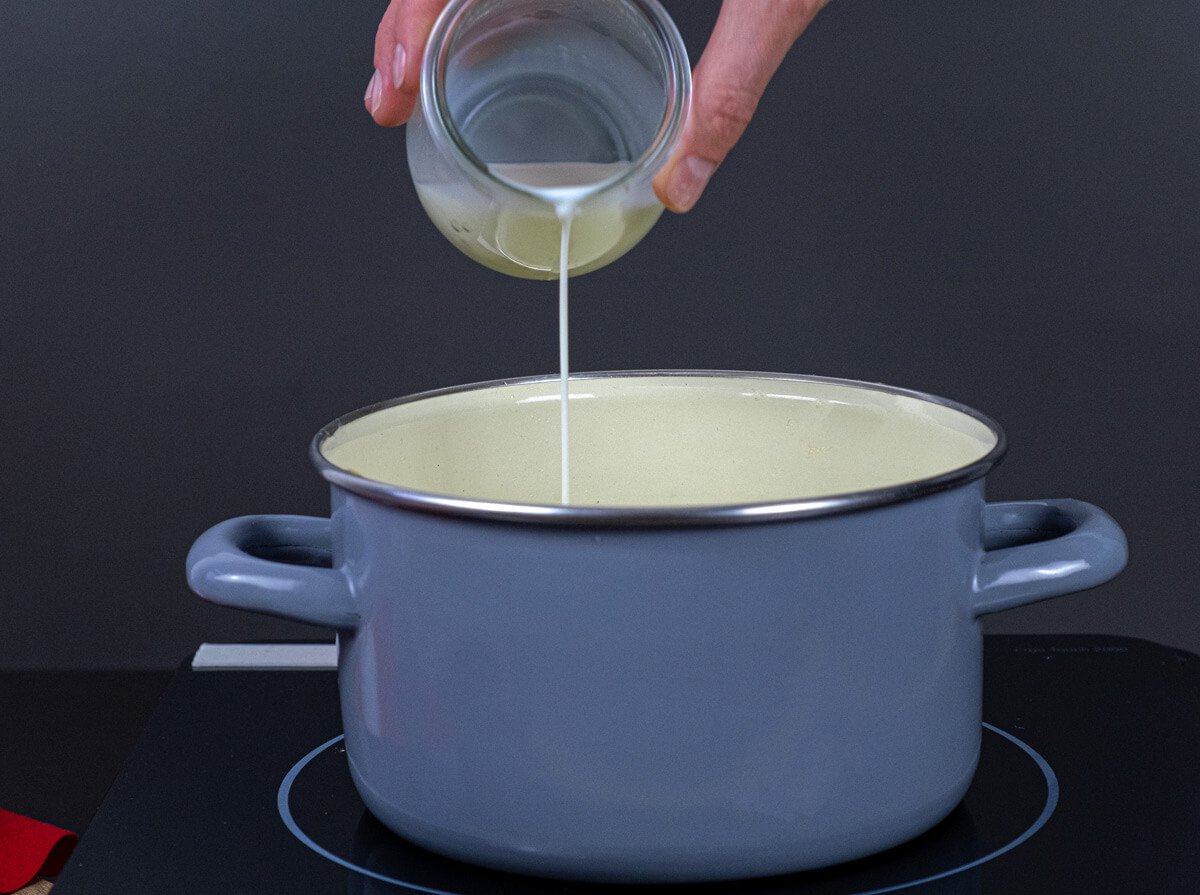 A hand pouring cream into an enameled Dutch oven.