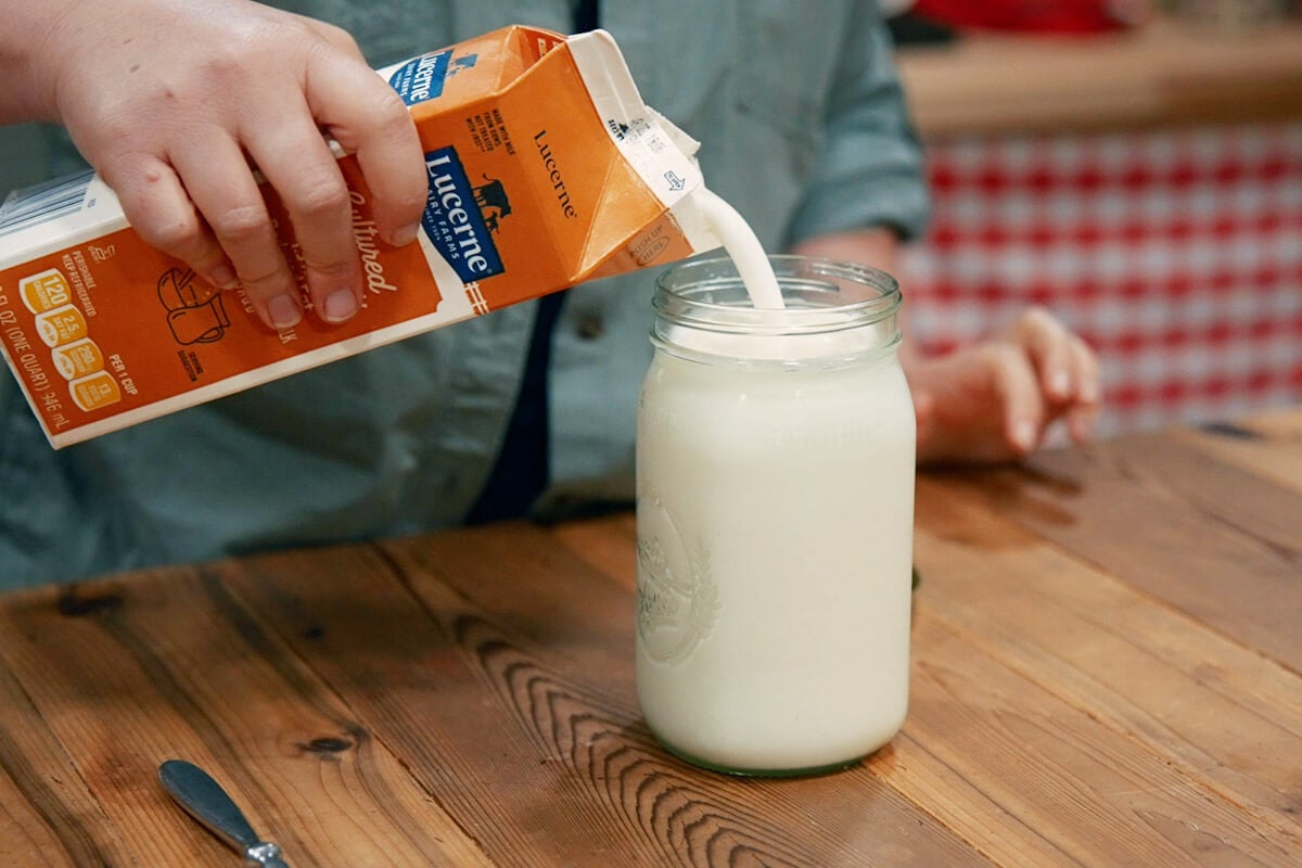 Hand pouring buttermilk into a glass jar of milk.