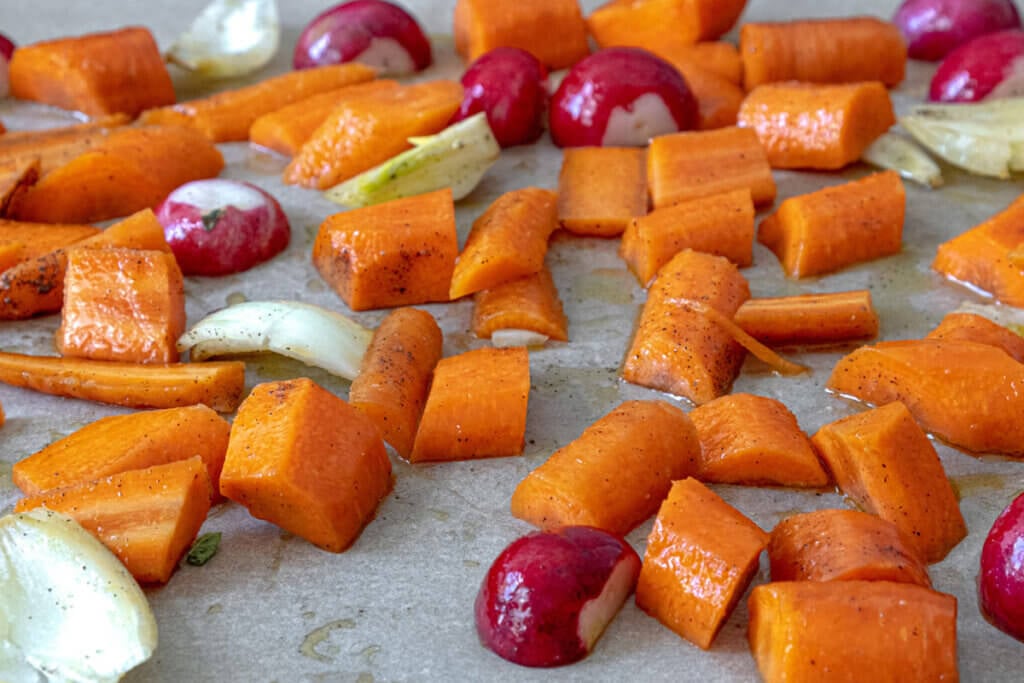Chopped carrots, radishes and onions on a roasting pan.