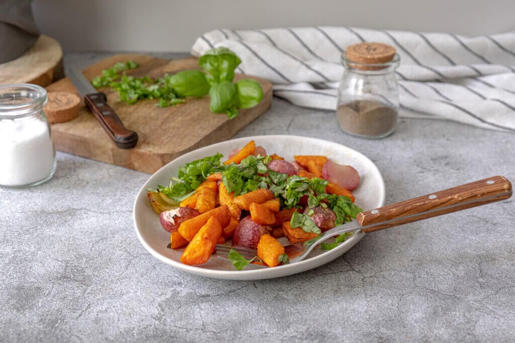 Roasted radishes and carrots on a plate garnished with fresh herbs.