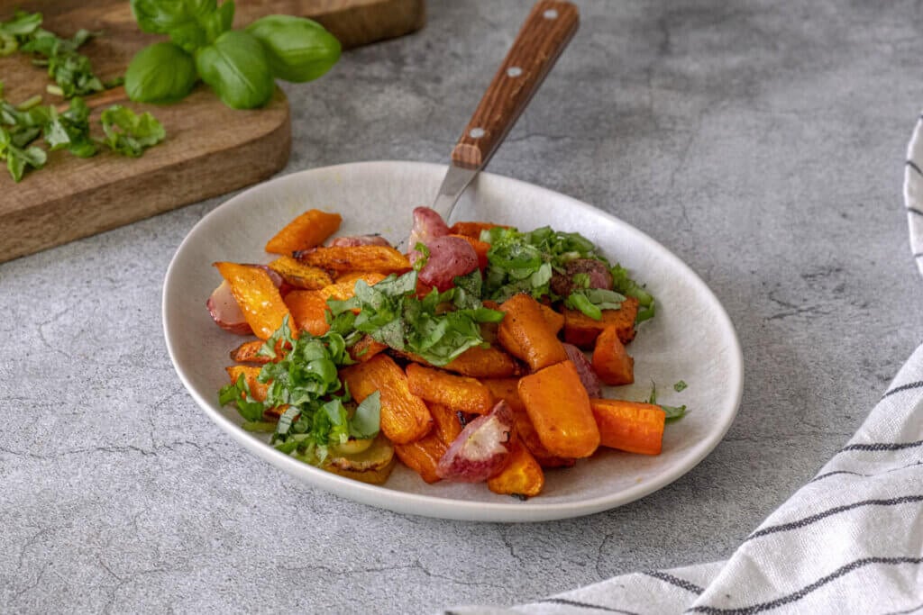 Roasted radishes and carrots on a plate garnished with fresh herbs.