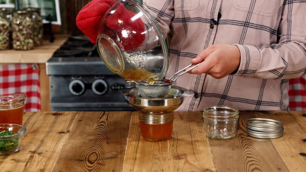 Herbal honey being strained into a jar.