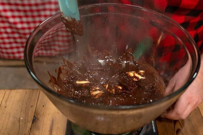 A double boiler with a glass bowl of chocolate and butter being stirred and melted.