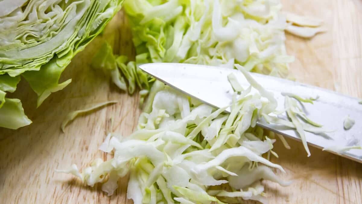 Sliced cabbage and large knife on a wooden cutting board.