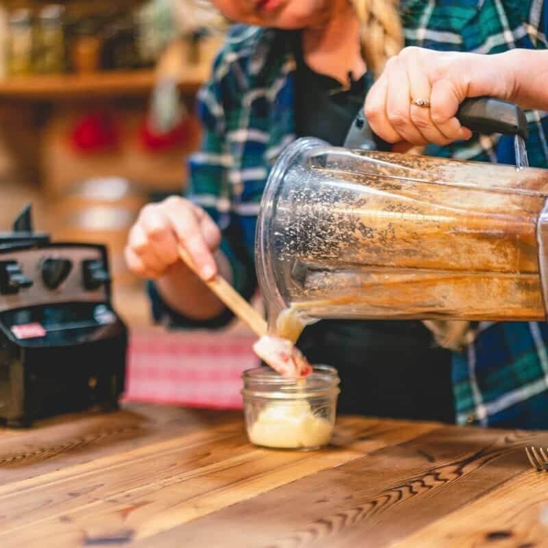Woman pouring garlic salve from a blender into a small glass jar.