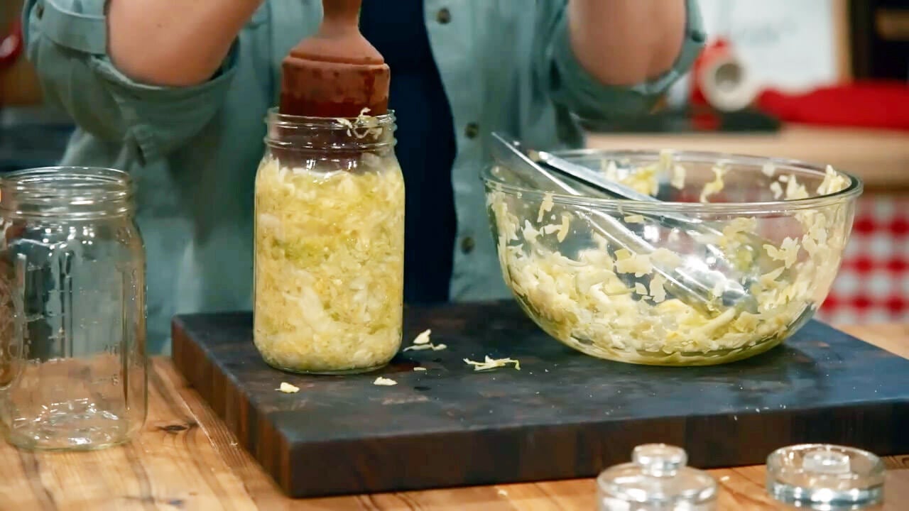 Packing shredded and salted cabbage into a jar with a kraut pounder.