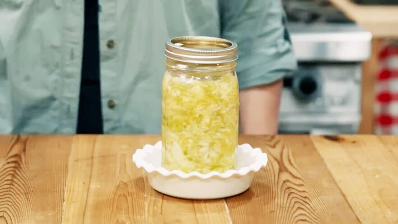 A glass jar full of shredded cabbage sitting in a baking dish ready to ferment.