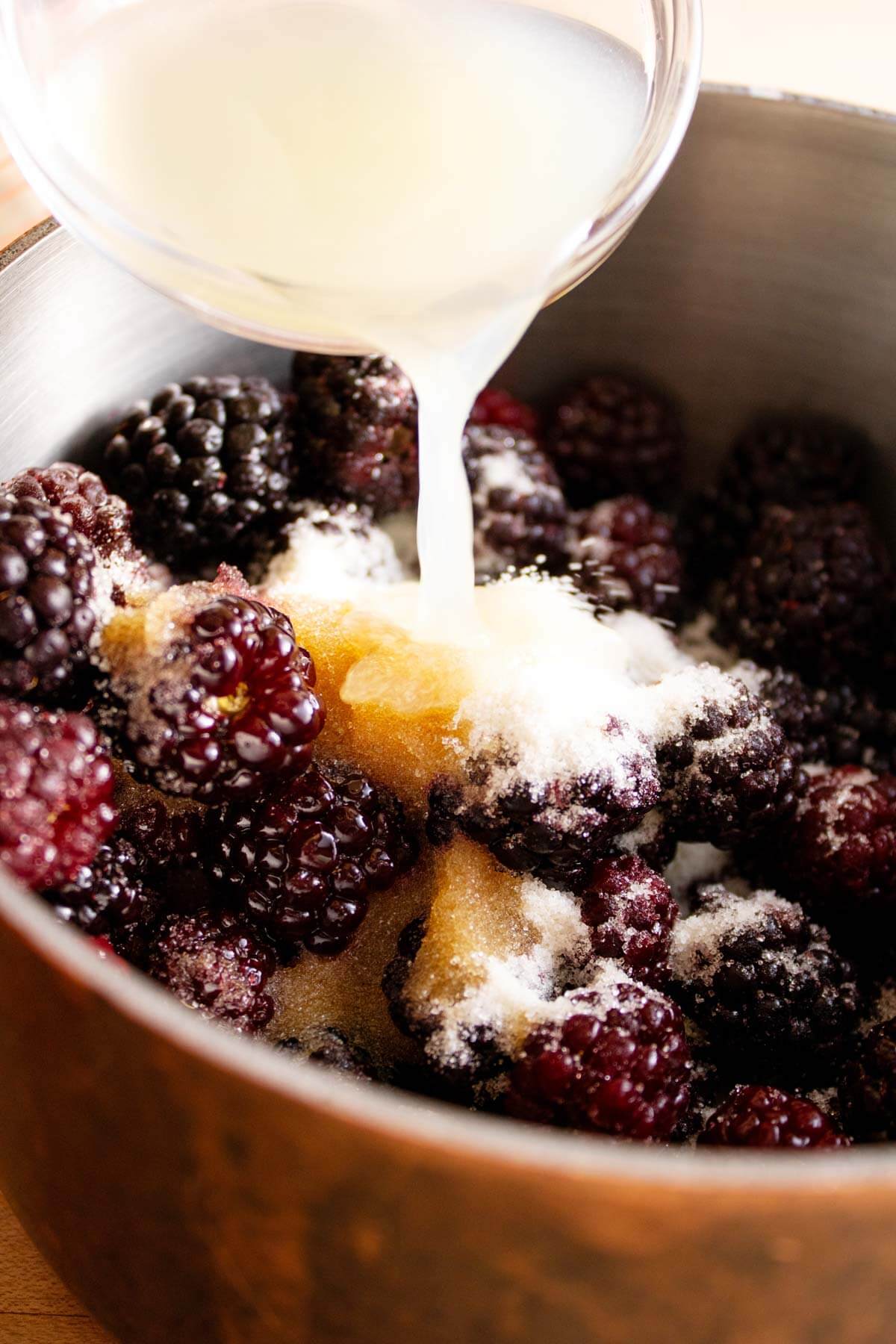 Pouring lemon juice out of a measuring dish into a saucpan of blackberry sauce.