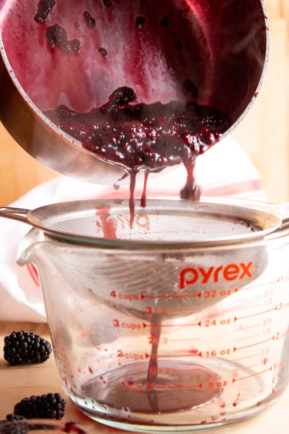 Blackberry sauce pouring out of a saucepan through a metal seive.