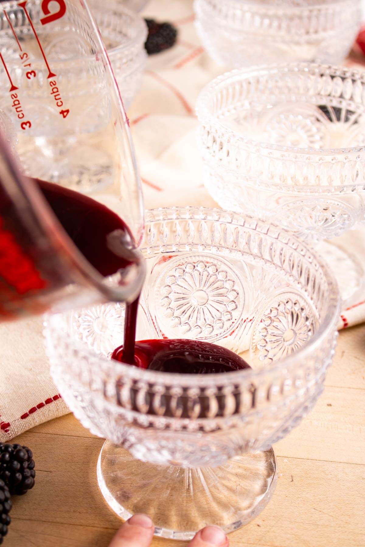 Blackberry sauce being poured into a stemware glass.