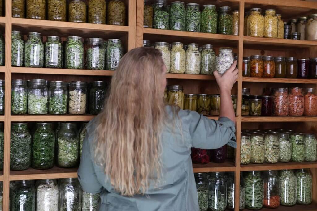 A woman putting a jar of food into a food storage pantry.