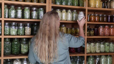 A woman putting a jar of food into a food storage pantry.