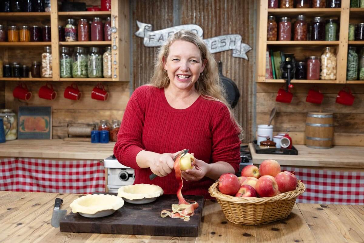 A woman peeling apples to make an apple pie.