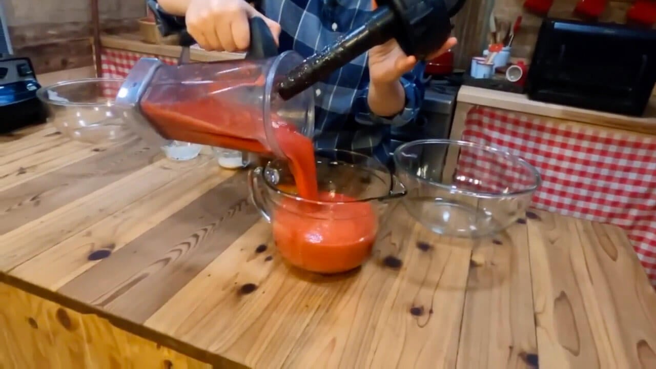 Hands pouring fruit puree from a blender into a bowl.
