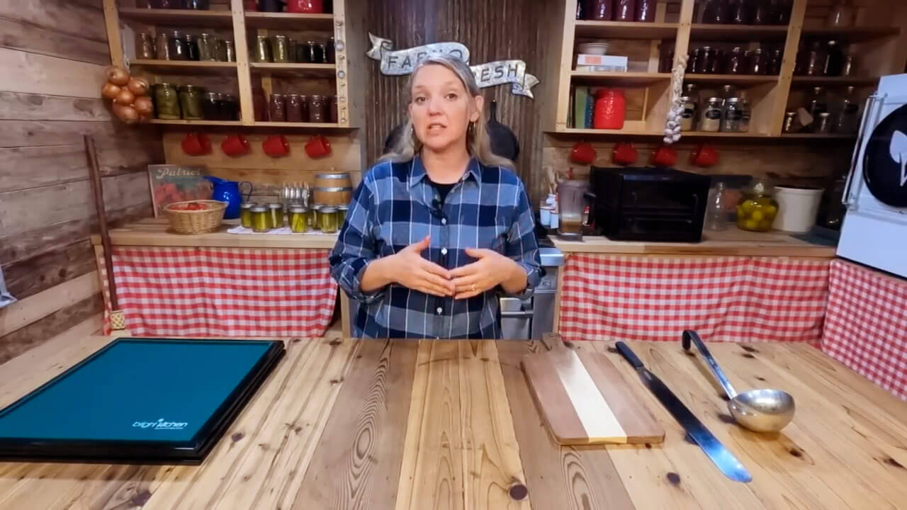 A woman standing in front of fruit leather freeze drying supplies: lined dehydrator trays, a ladle, spatula, and cutting board.