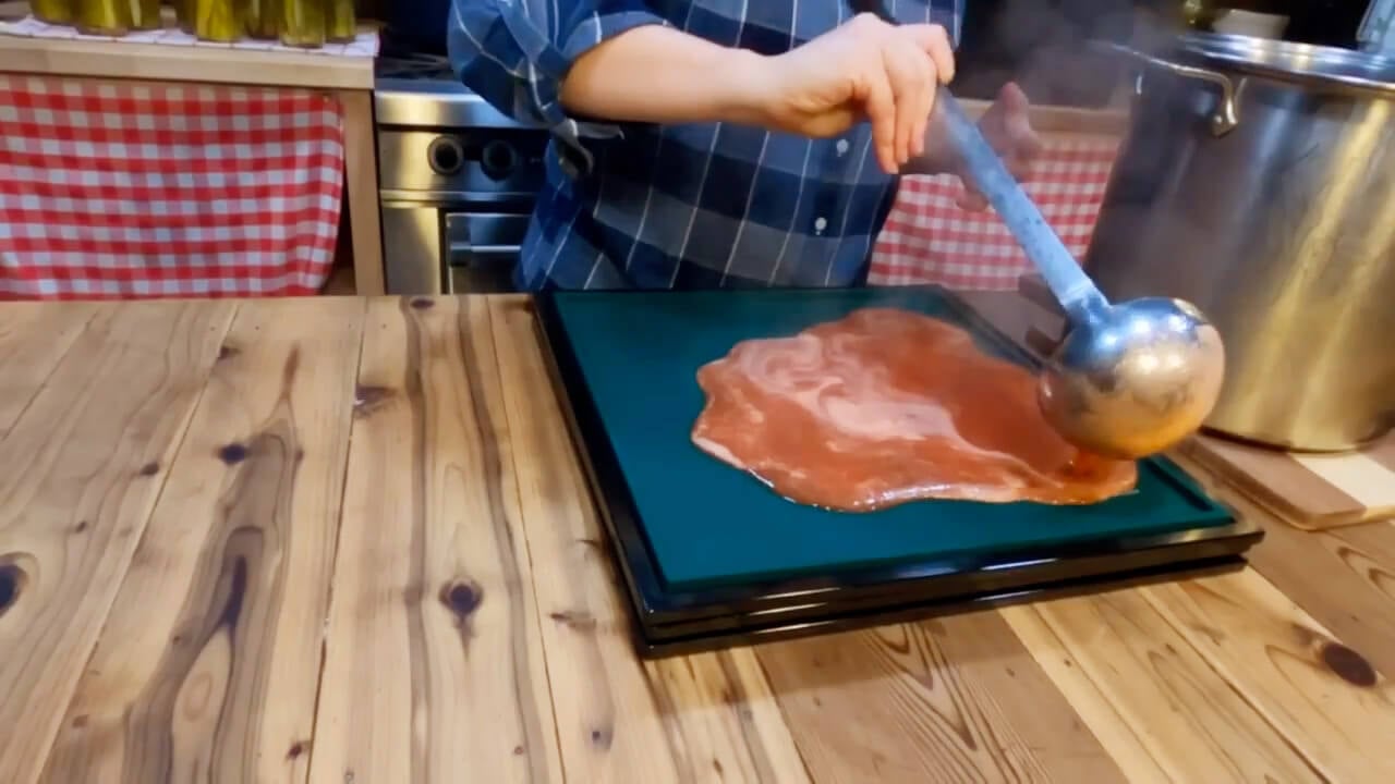 Hands ladling prepared fruit pureé onto dehydrator trays.