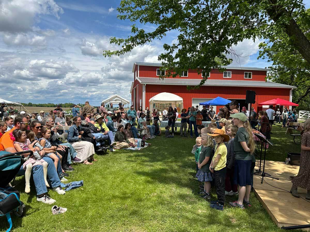 A large gathering of people with a red barn in the background.