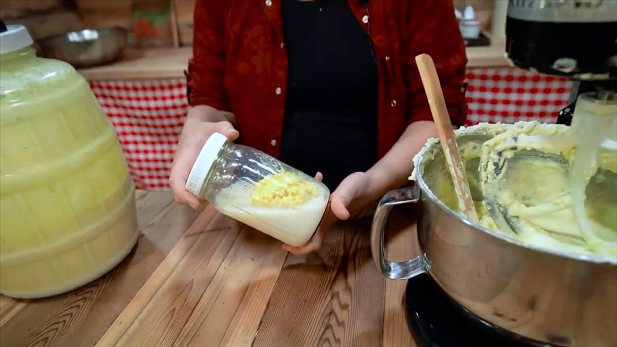 Hands holding a jar of butter solids that have separated from the buttermilk.