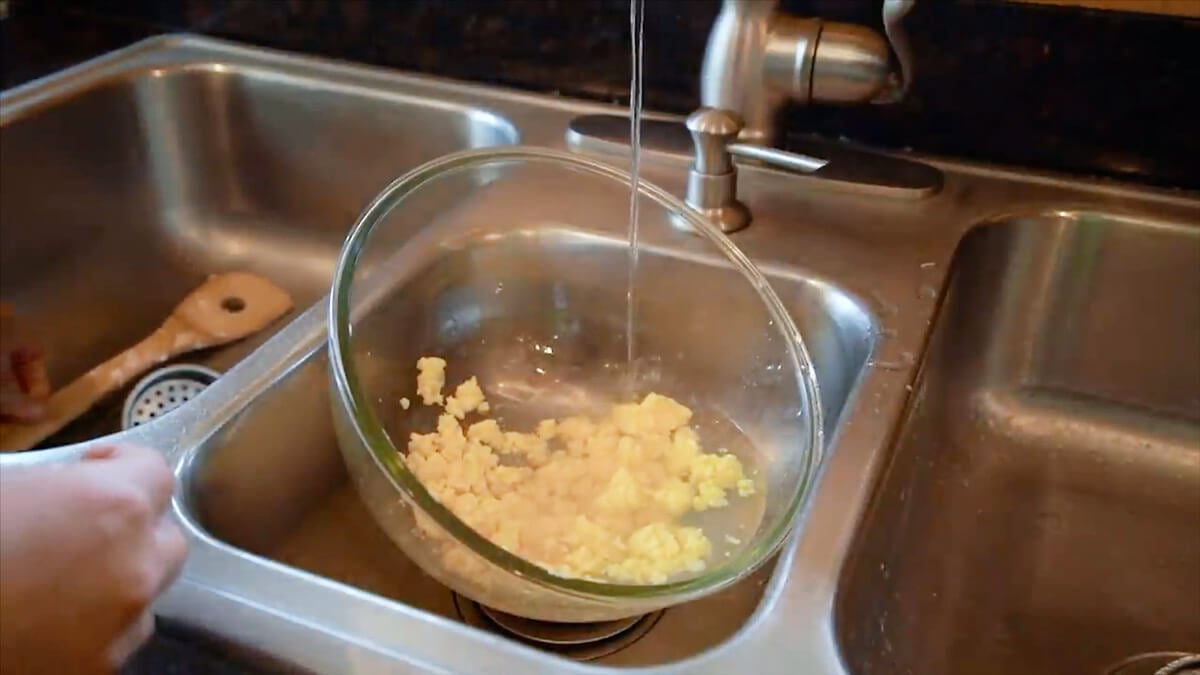 A bowl of freshly churned butter being rinsed under running water to remove remaining buttermilk.