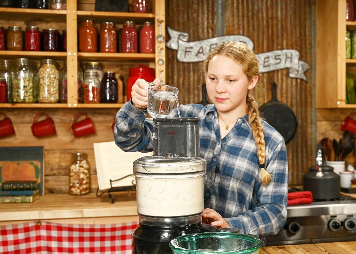 A young woman pouring ice water into a food processor.