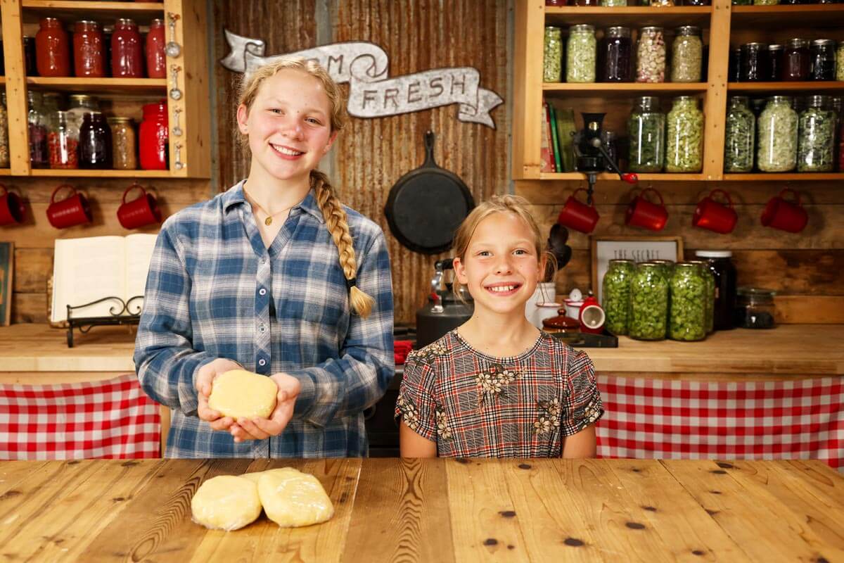 Two young girls holding up homemade pie crust.