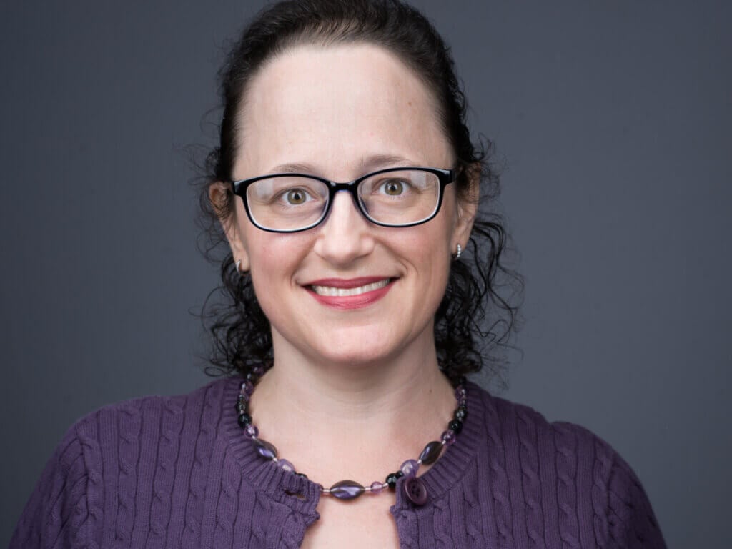 Headshot of a woman in a purple shirt and glasses.