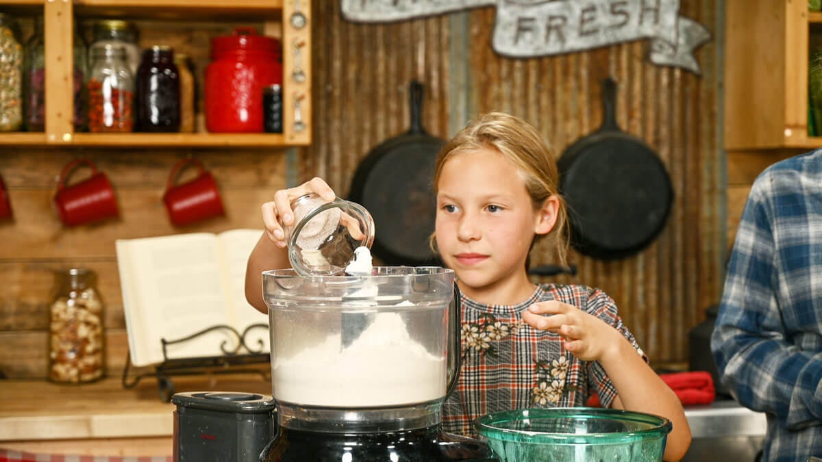 A young girl adding salt to a food processor.