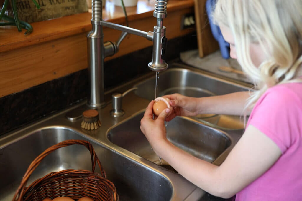 A young girl washing an egg in the sink.