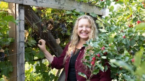 A woman standing by a grapevine.