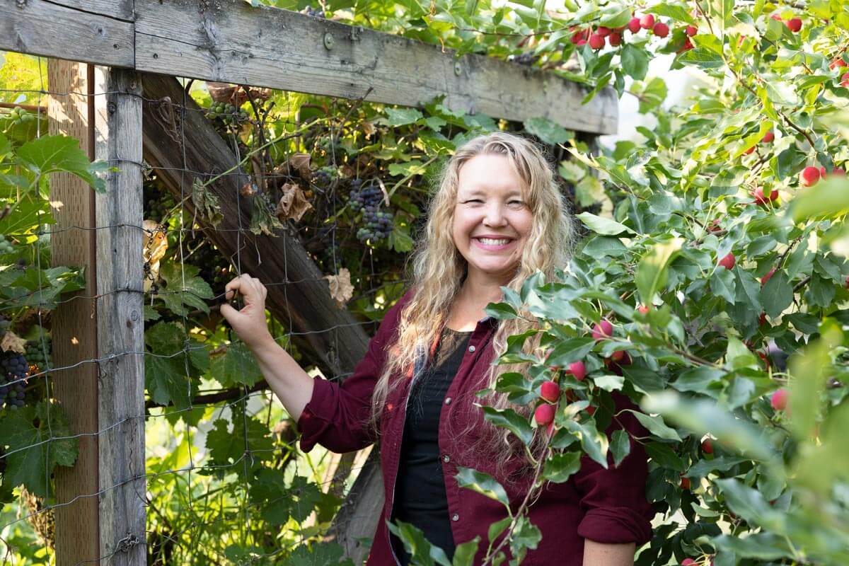 A woman standing by a grapevine.