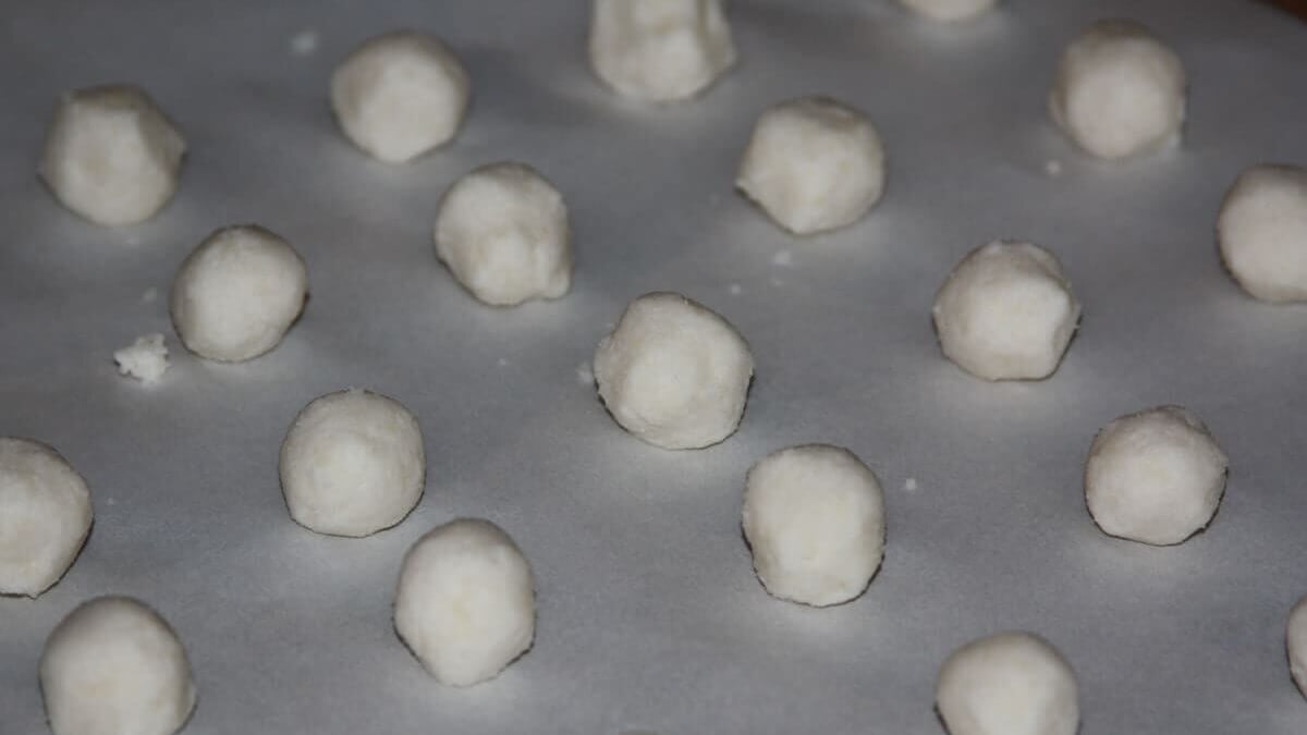 Coconut truffle balls on a cookie sheet lined with parchment paper.