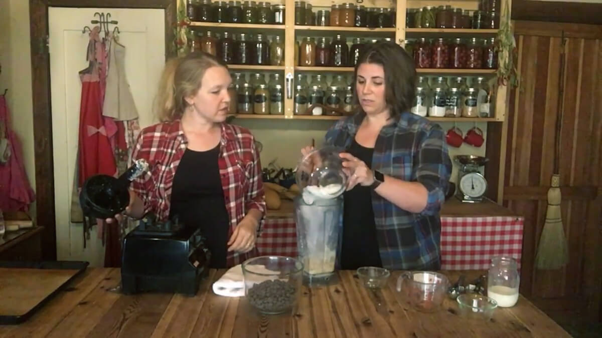 A woman adding coconut flakes to a blender.