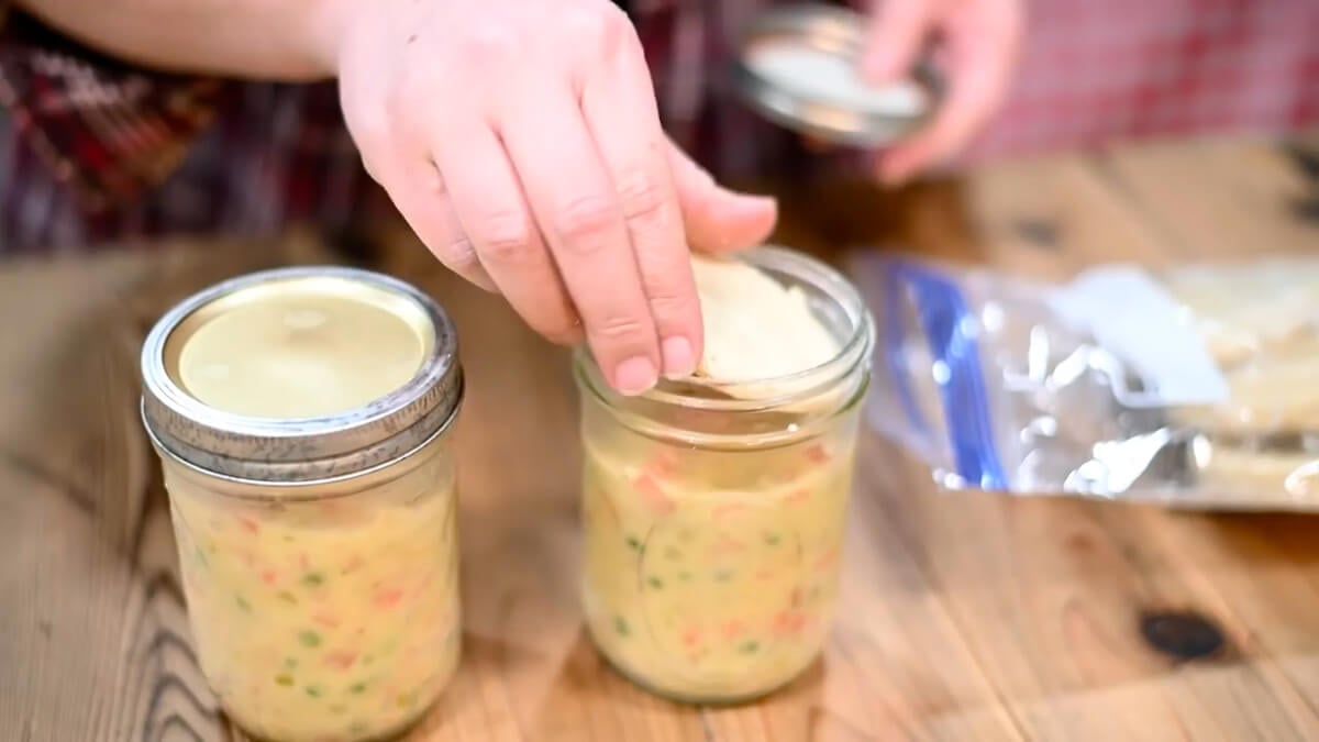 Hands placing pot pie crust on the top of pot pie filling in a jar.
