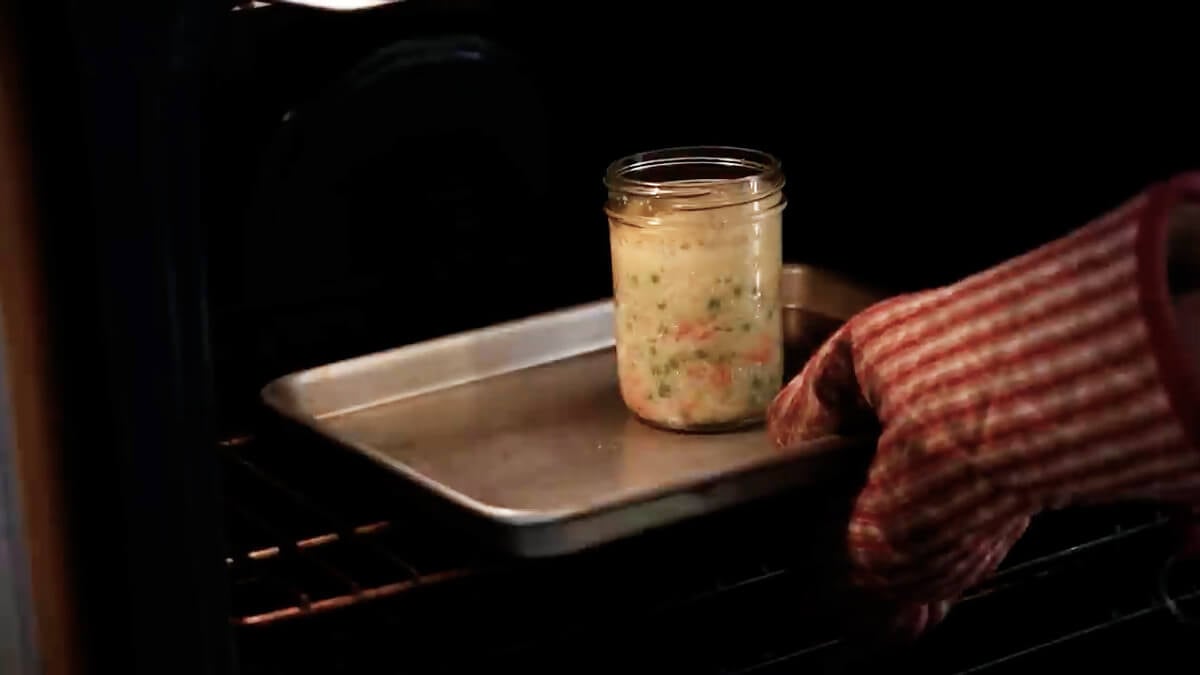 Hands placing a jar of chicken pot pie sitting on a cookie sheet in the oven.