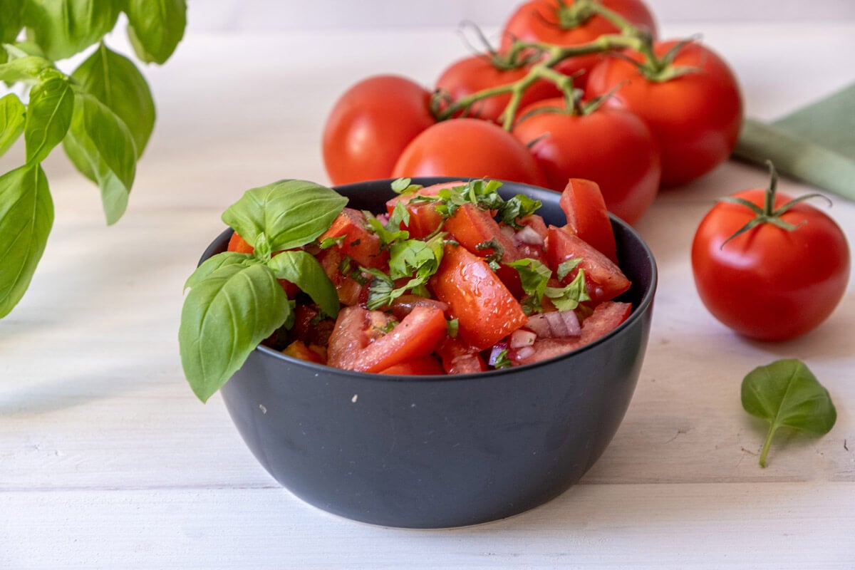 Tomato and onion salad served in a black bowl and garnished with fresh basil leaves.