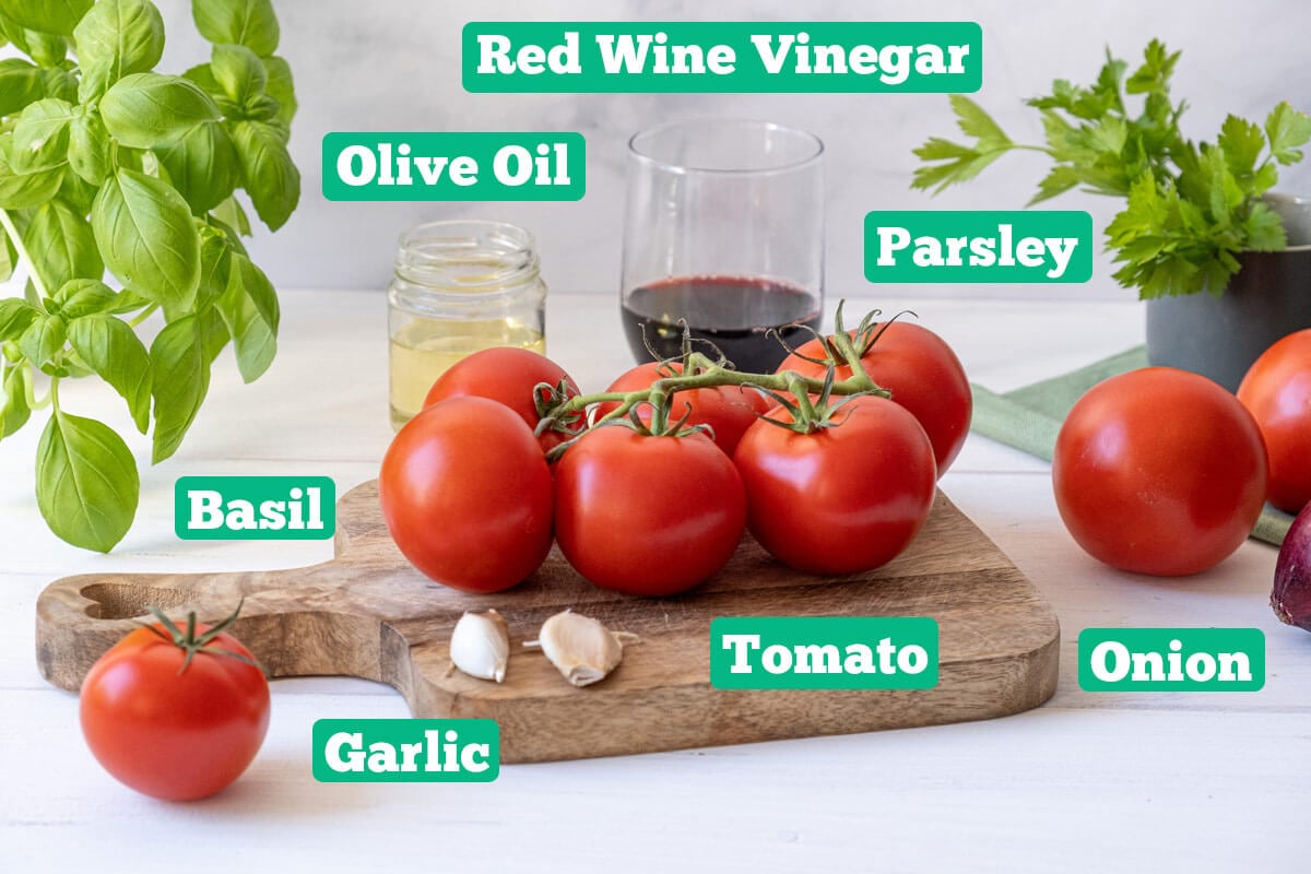 Tomato onion salad ingredients: red wine vinegar, olive oil, parsley, basil, tomato, onion, and garlic.