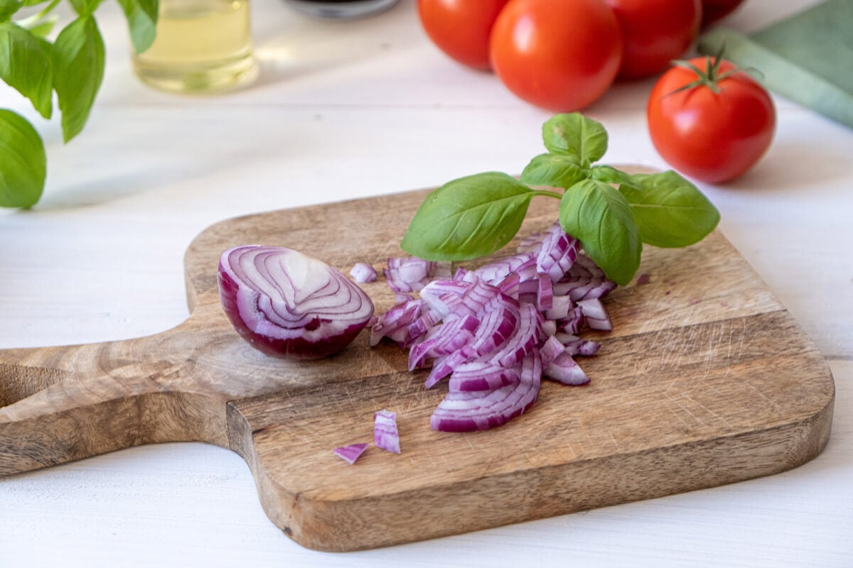 Diced red onion on a cutting board with fresh basil leaves.