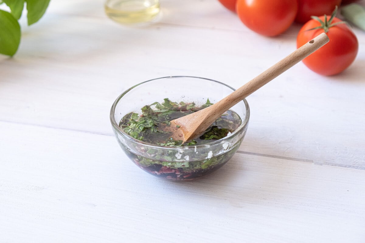 Fresh herbs and vinaigrette dressing in a mixing bowl.