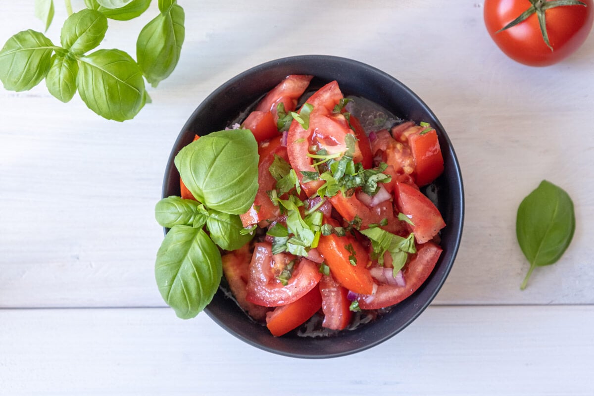 Bird's eye view of tomato and onion salad served in a black bowl and garnished with fresh basil leaves.
